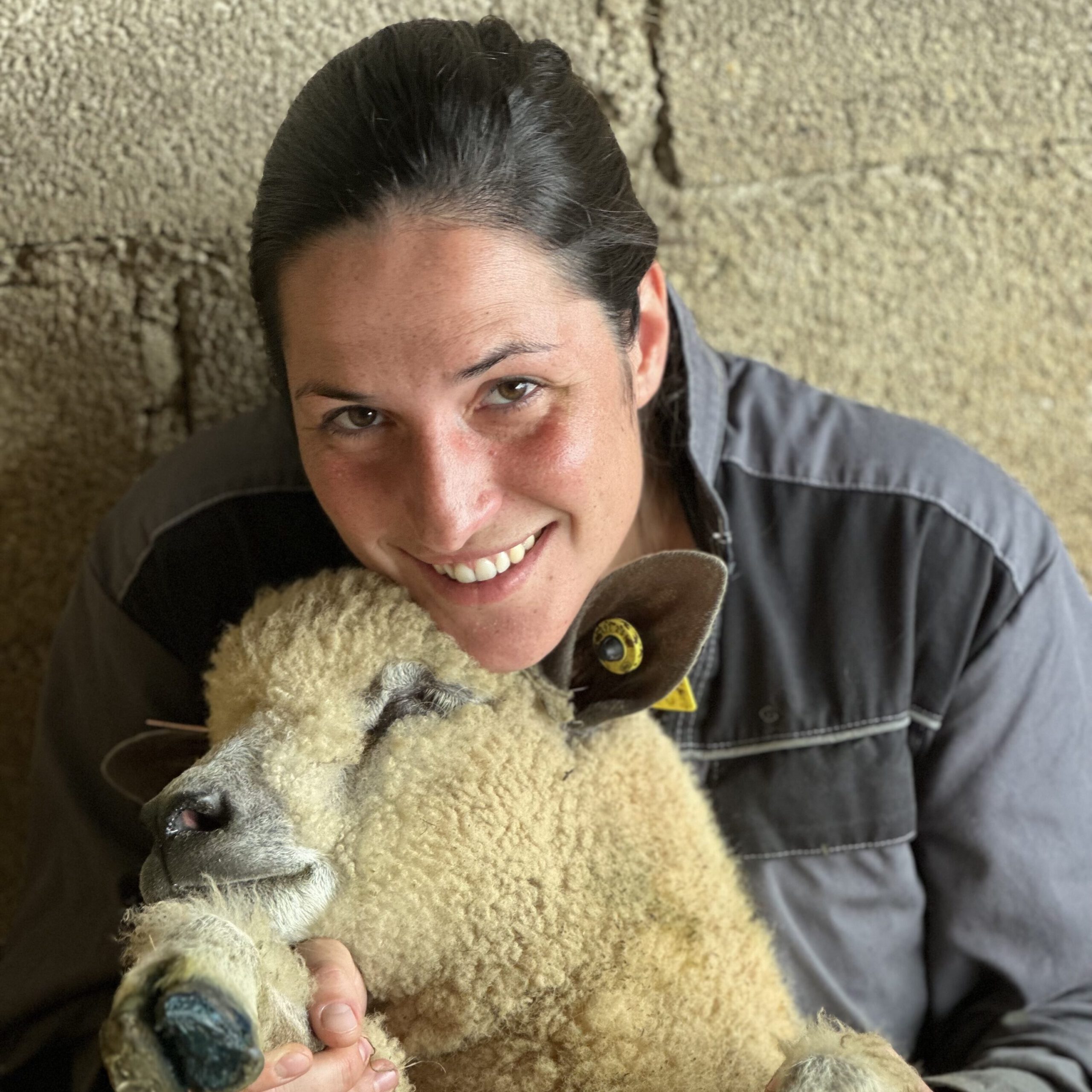 Portrait d'une femme souriante tenant un mouton dans un environnement naturel, illustrant l'engagement de "Laines sous les Pommiers".