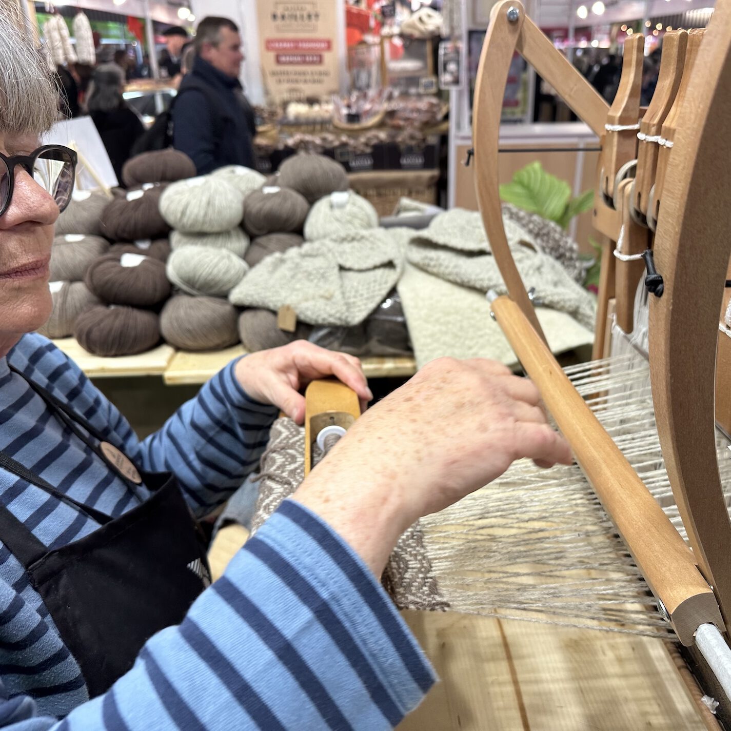 Femme tissant de la laine sur un métier, entourée de pelotes et de vêtements en laine, représentant l'artisanat durable.