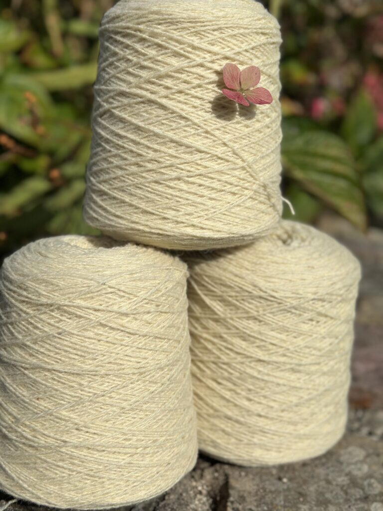 Trois pelotes de laine claire empilées, ornées d'une petite fleur, sur un fond naturel.