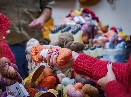 Main tenant une pelote de laine parmi d'autres, dans un environnement d'artisanat coloré.