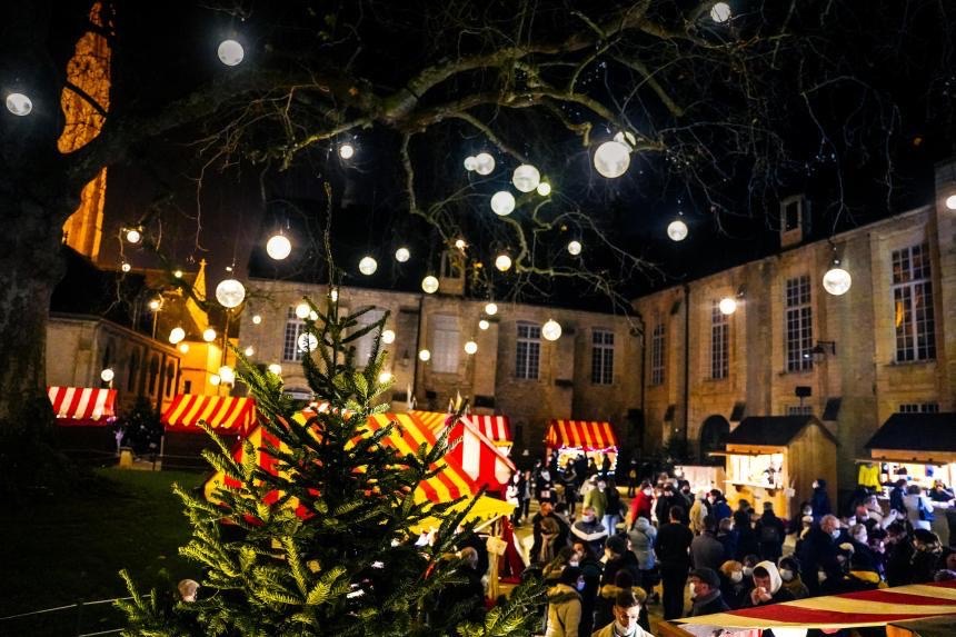 Marché nocturne sous des lampions avec des stands colorés, ambiance festive et arbres décorés.