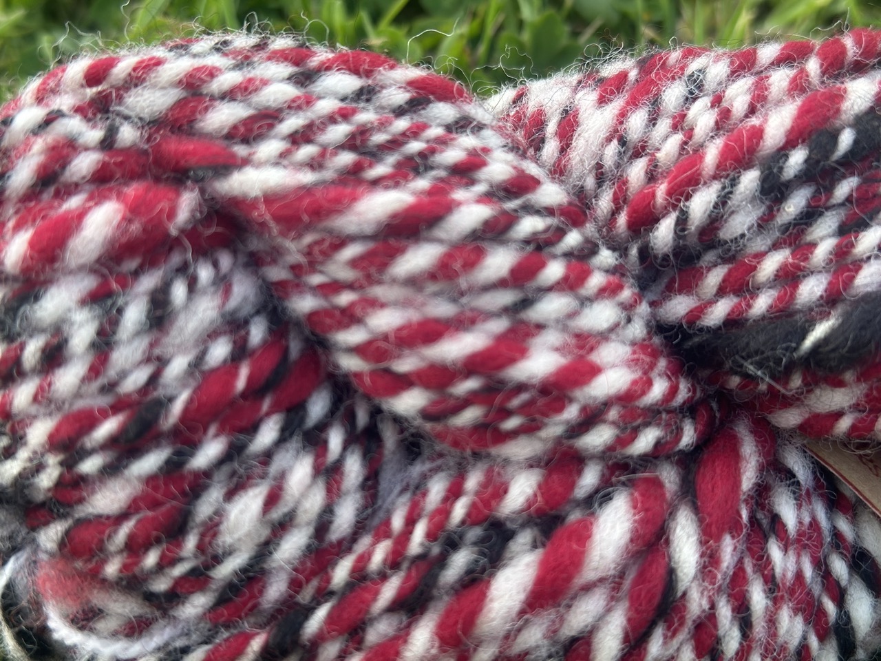 Écheveaux de laine filée main en rouge, noir et blanc, produits par "Laines sous les Pommiers". Artisanat normand durable.