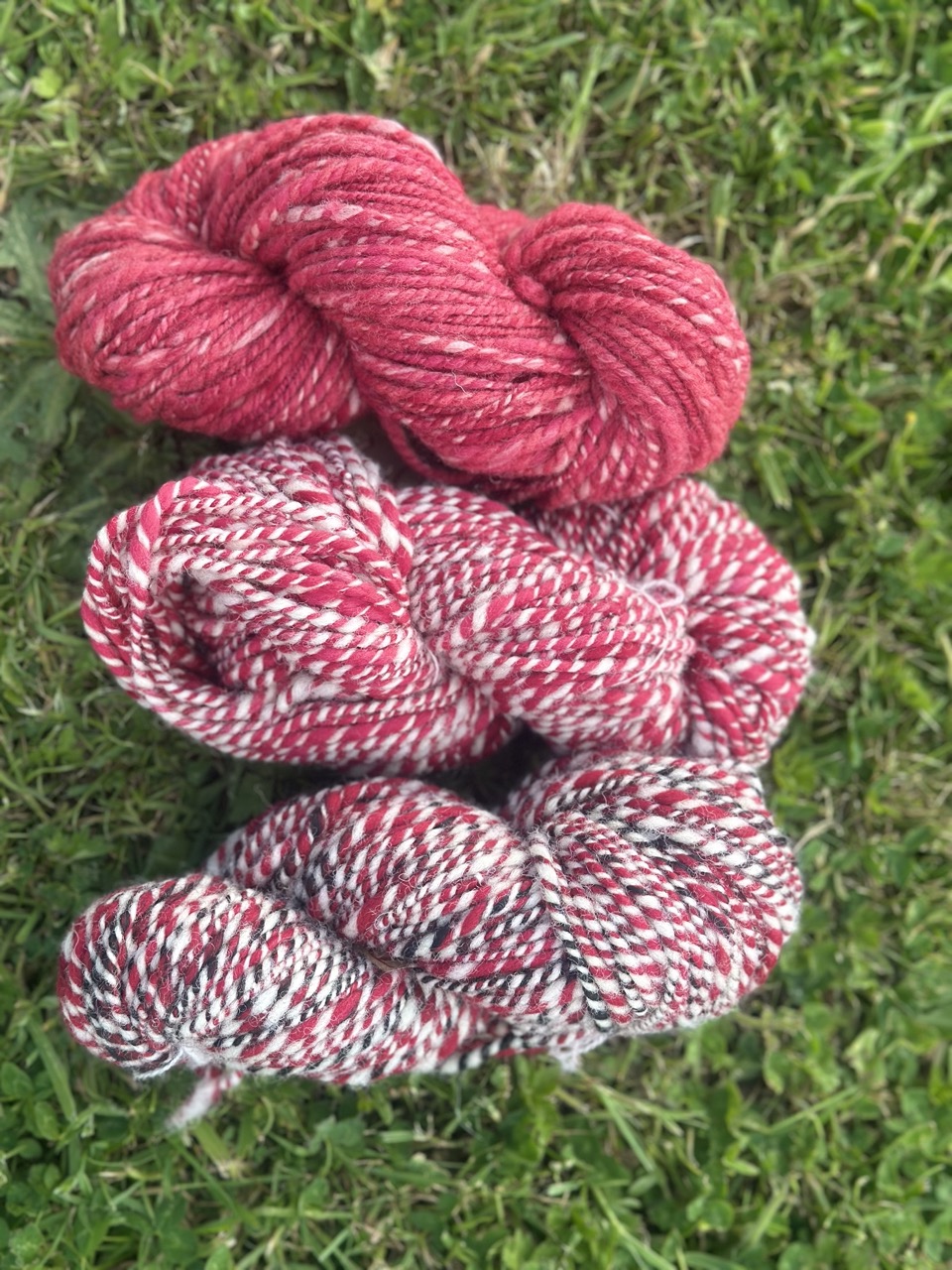 Écheveaux de laine filée main en rouge et motifs, signés Rouge Garance, sur un fond de gazon.
