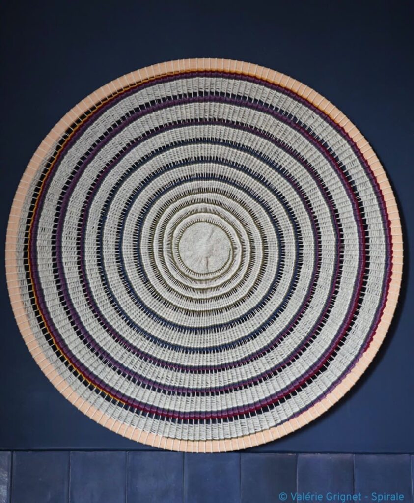 Artisanat français : tissage rond en laine, présentant des motifs concentriques sur fond bleu.