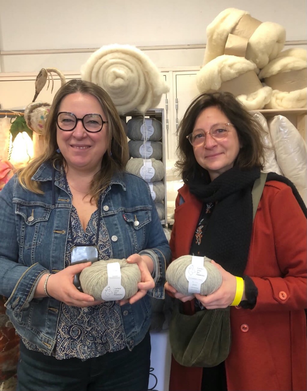 Deux femmes souriantes tenant des pelotes de laine de la marque normande Laines sous les Pommiers, entourées de produits artisanaux.